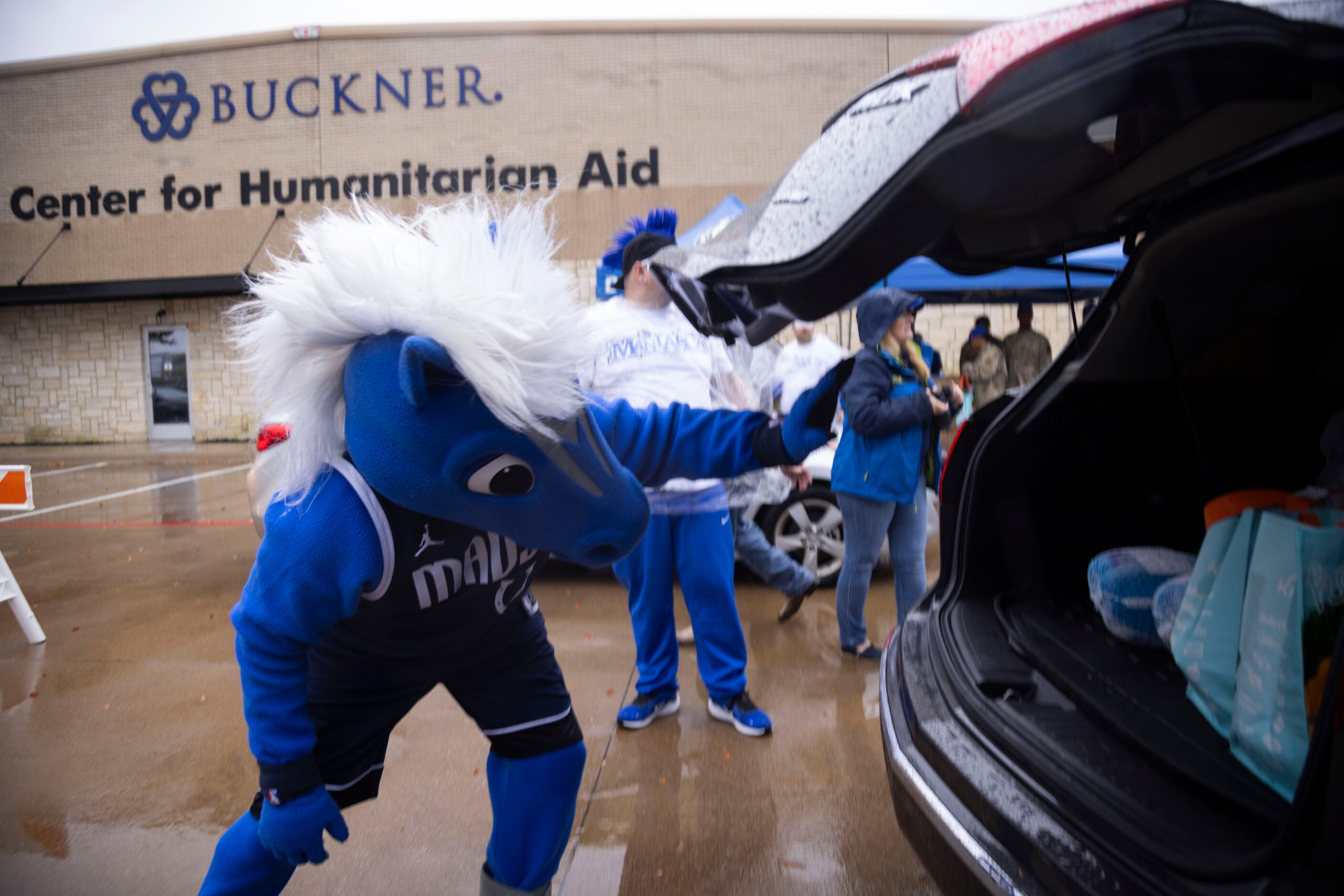 Champ, the Dallas Mavericks mascot, waves to a driver after loading a car during the Hoops...