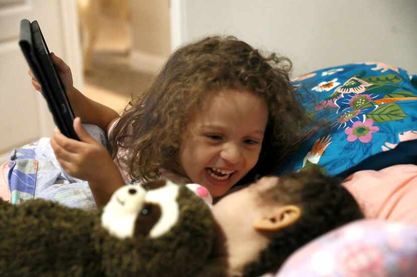 Lincoln Brooks, 4, smiles at older sister Charlotte, 5, as she selects a show for the two to...