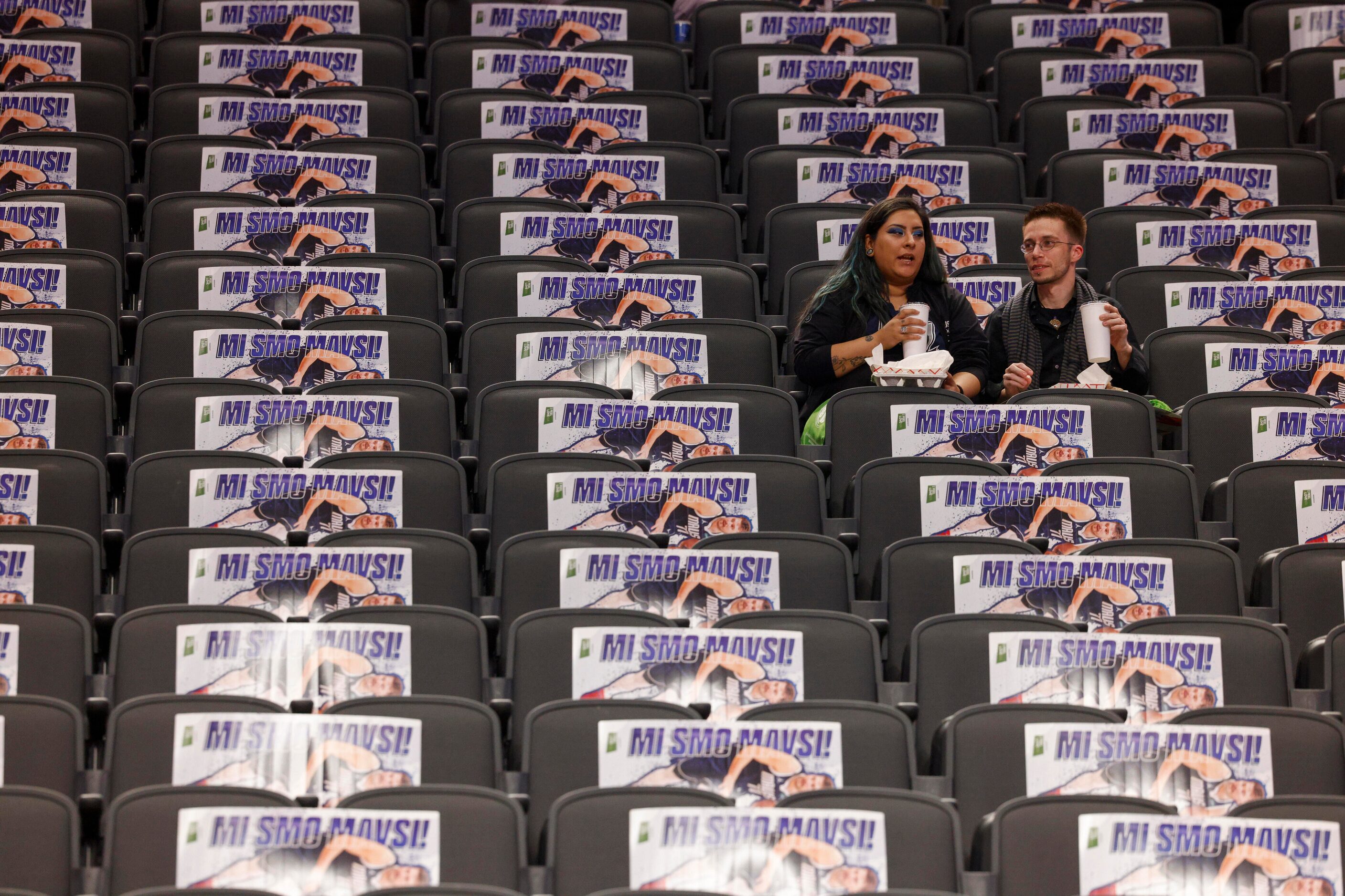 A pair of fans sit amongst a Slovenian themed Dallas Mavericks guard Luka Doncic poster...