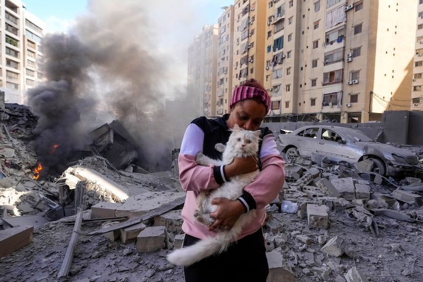 A woman holds her cat in front of a destroyed building at the site of an Israeli airstrike...