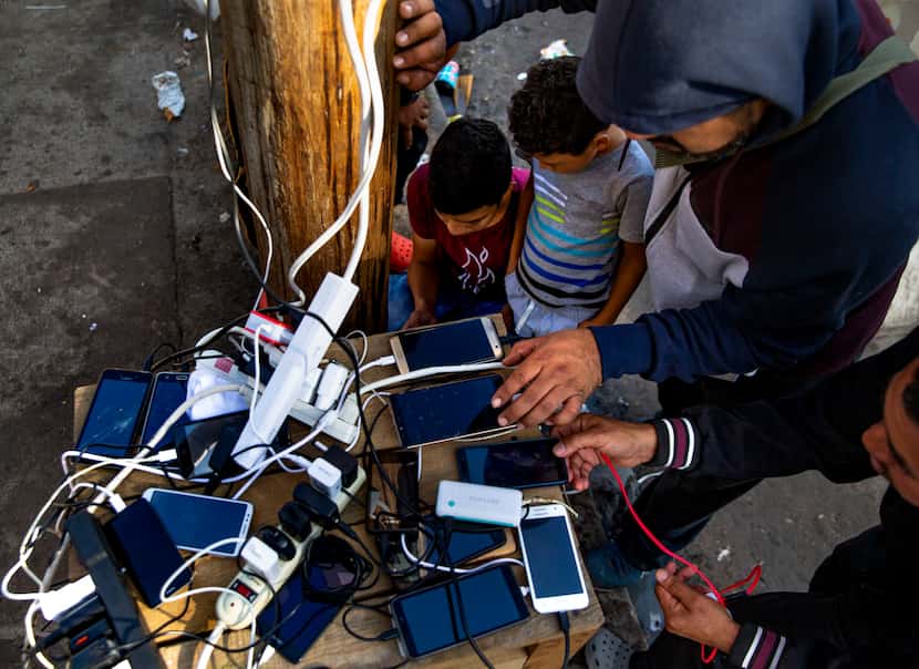 Asylum-seekers charge phones at the charging station at the temporary tent camps in...