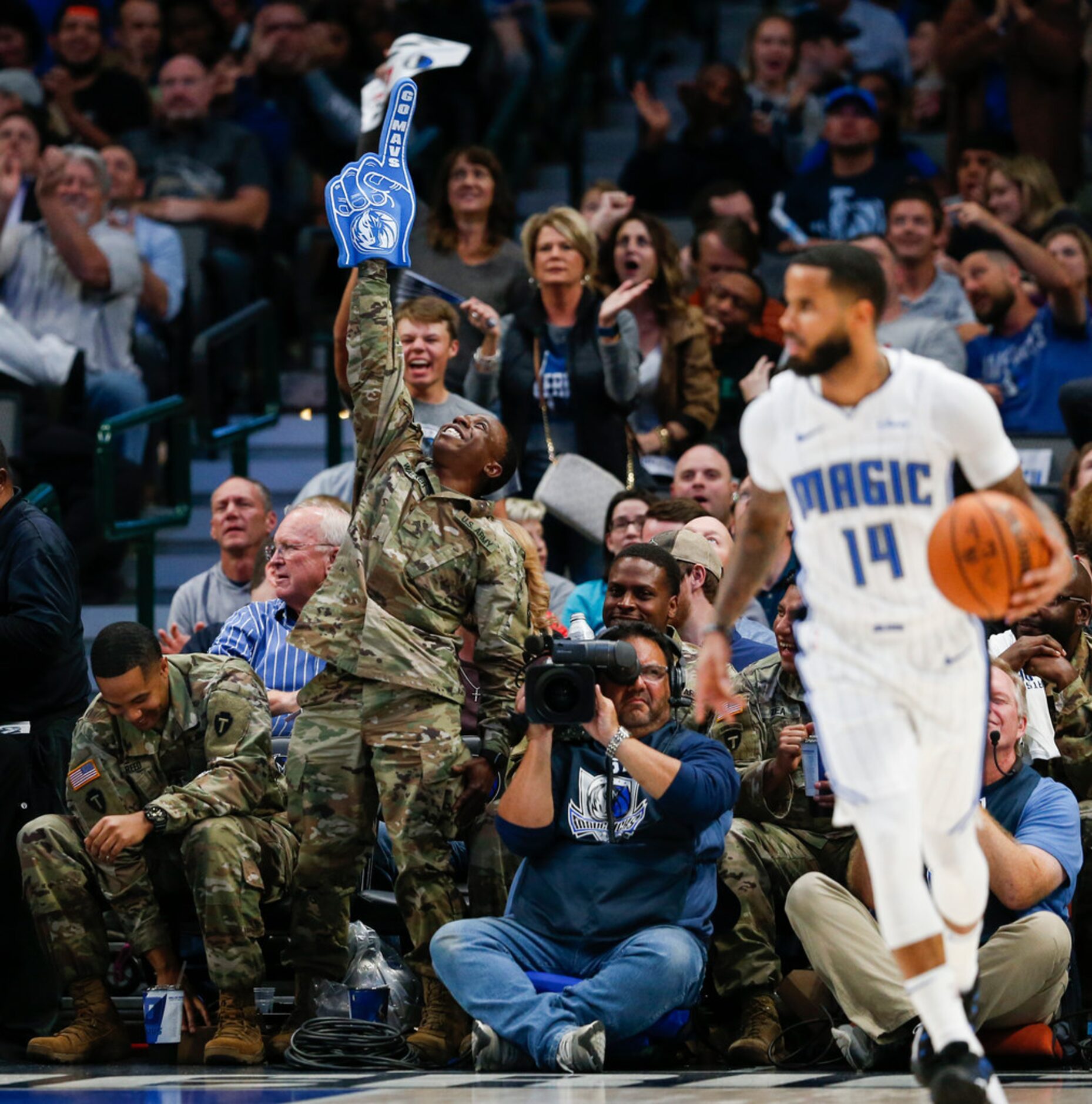 Armed forces members celebrate from the sidelines during the third quarter of an NBA game...