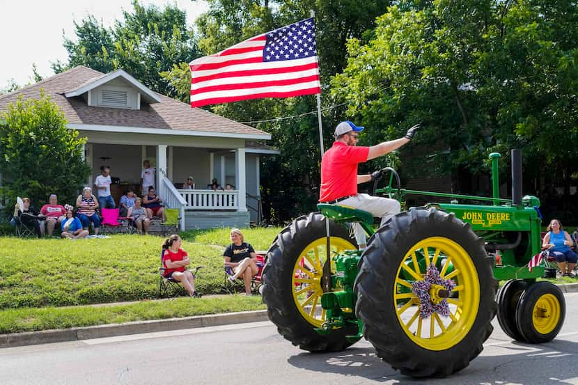 A man riding tall on a John Deere tractor waved to residents along the route of the...