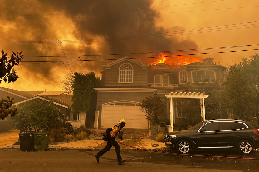 Una residencia en llamas mientras un bombero combate un incendio en Pacific Palisades, el...