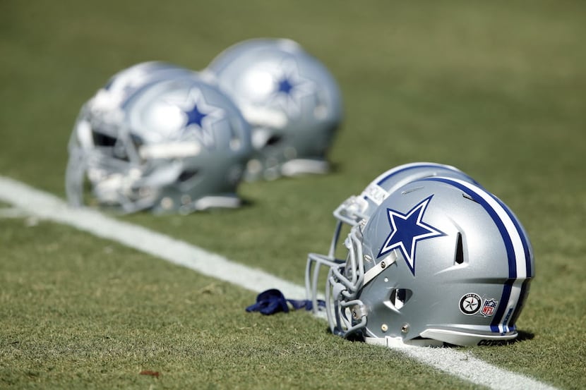 Dallas Cowboys players leave their helmets on the sideline as they walk thru plays before...