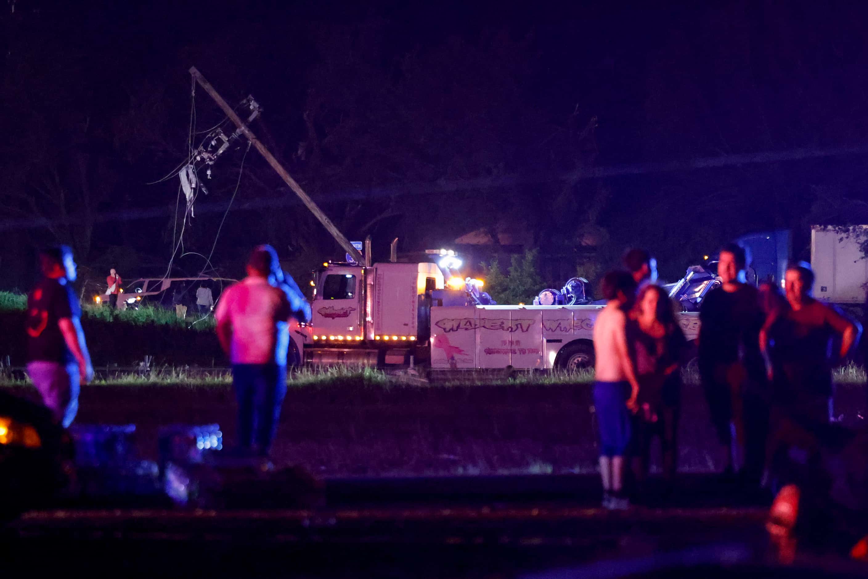People stand along Interstate 35 near a Shell gas station as  emergency crews tend to downed...