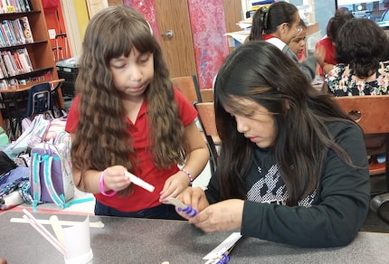 Two schoolgirls work on crafting a project at a craft table.