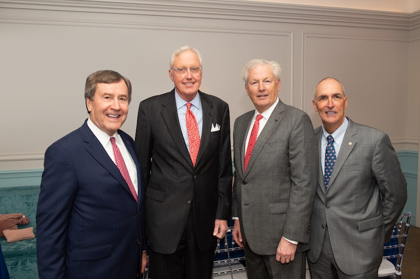 Four men in suits pose together inside SMU building.