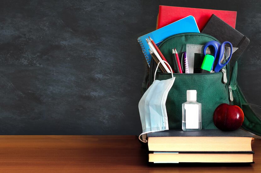 A backpack with school supplies, hand sanitizer, and a mask. Two books are stacked together...