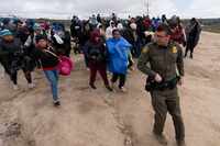 Solicitantes de asilo, incluido un grupo de peruanos, caminan detrás de un agente de la...