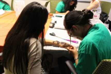  A volunteer paints a Henna design onto a student's hand at the Henna Painting event during...
