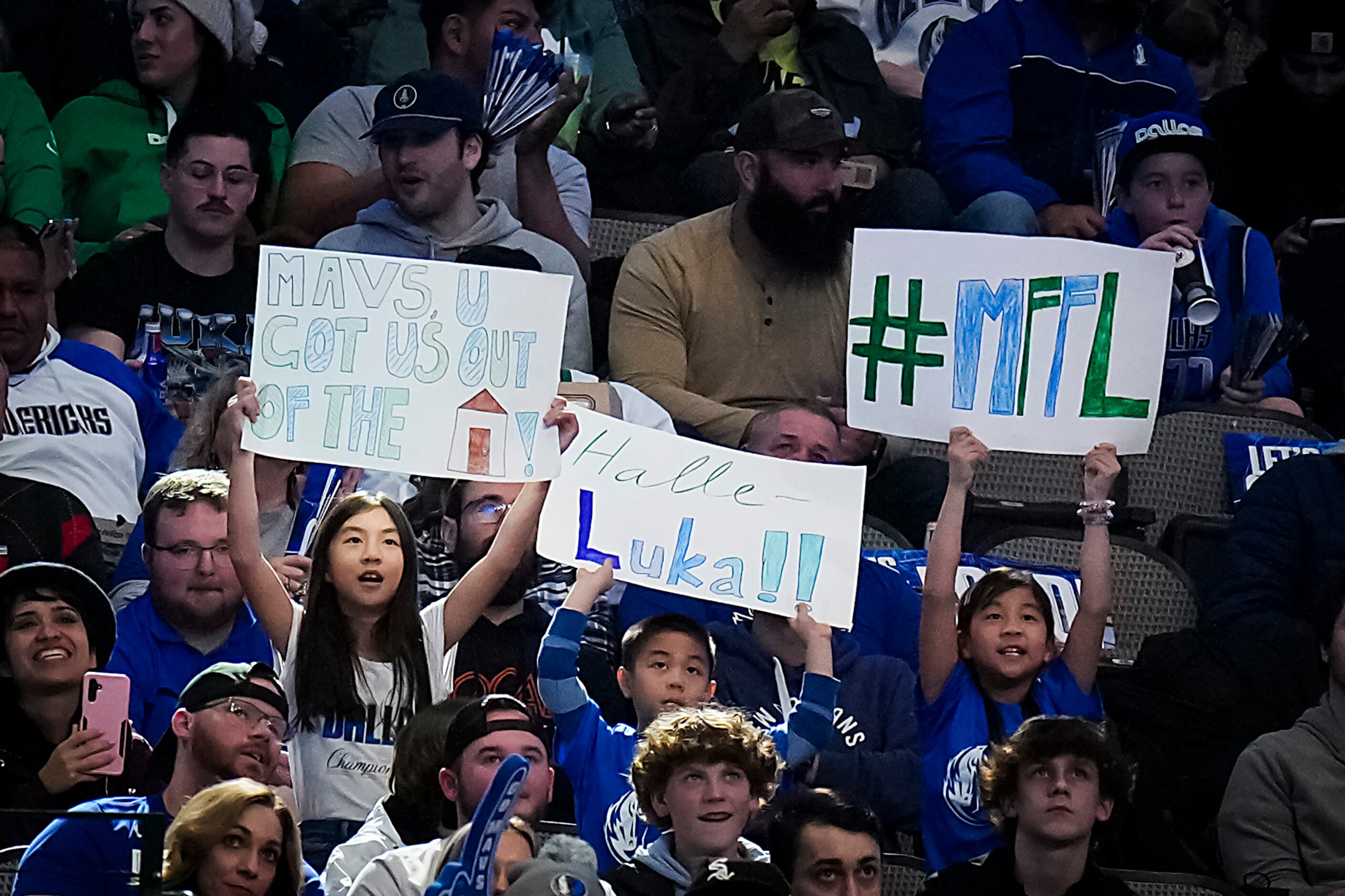 Dallas Mavericks fans hold up signs, including one referencing getting out of the house...