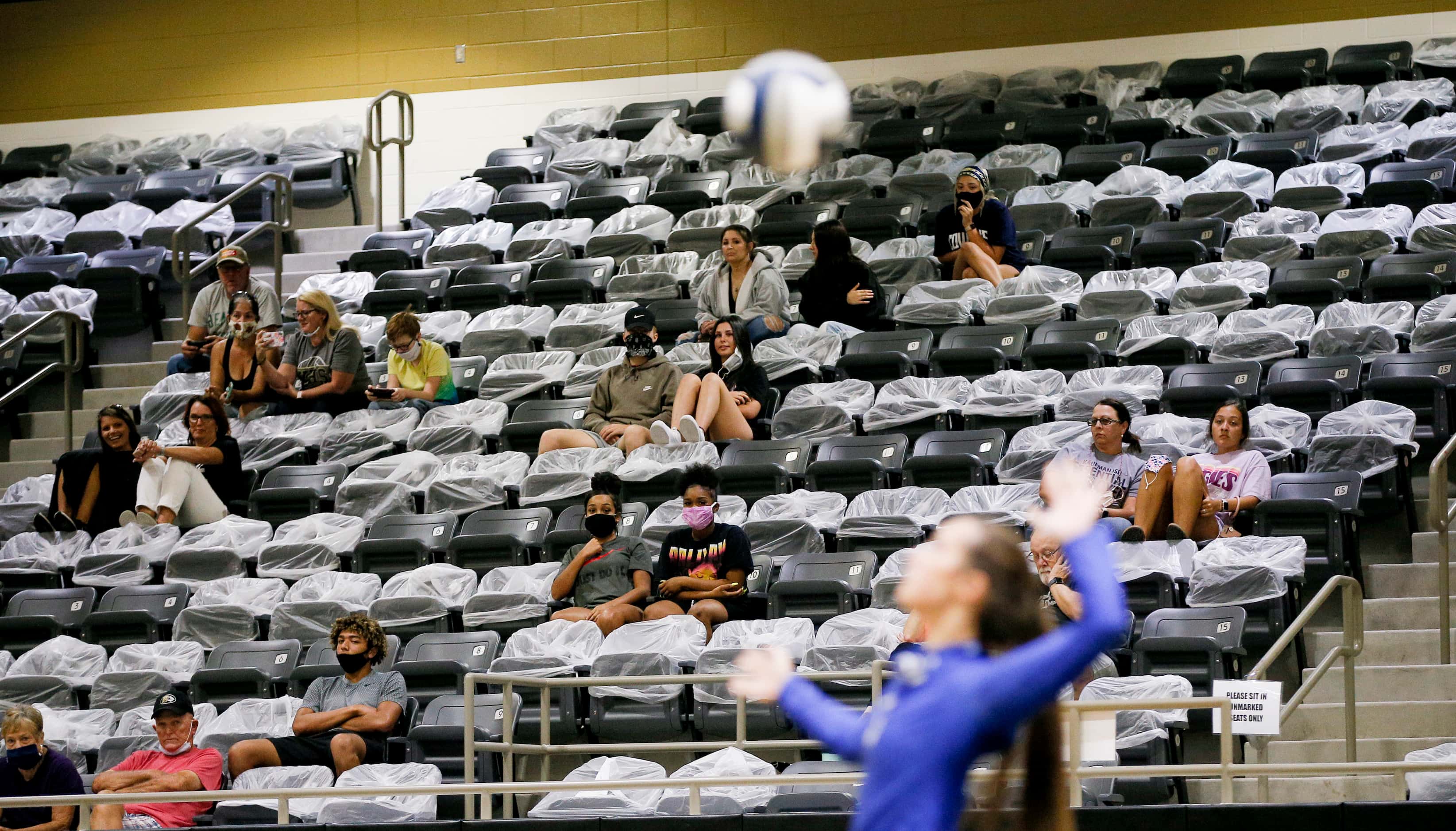 Volleyball spectators look on while social distancing with seats cordoned off with plastic...