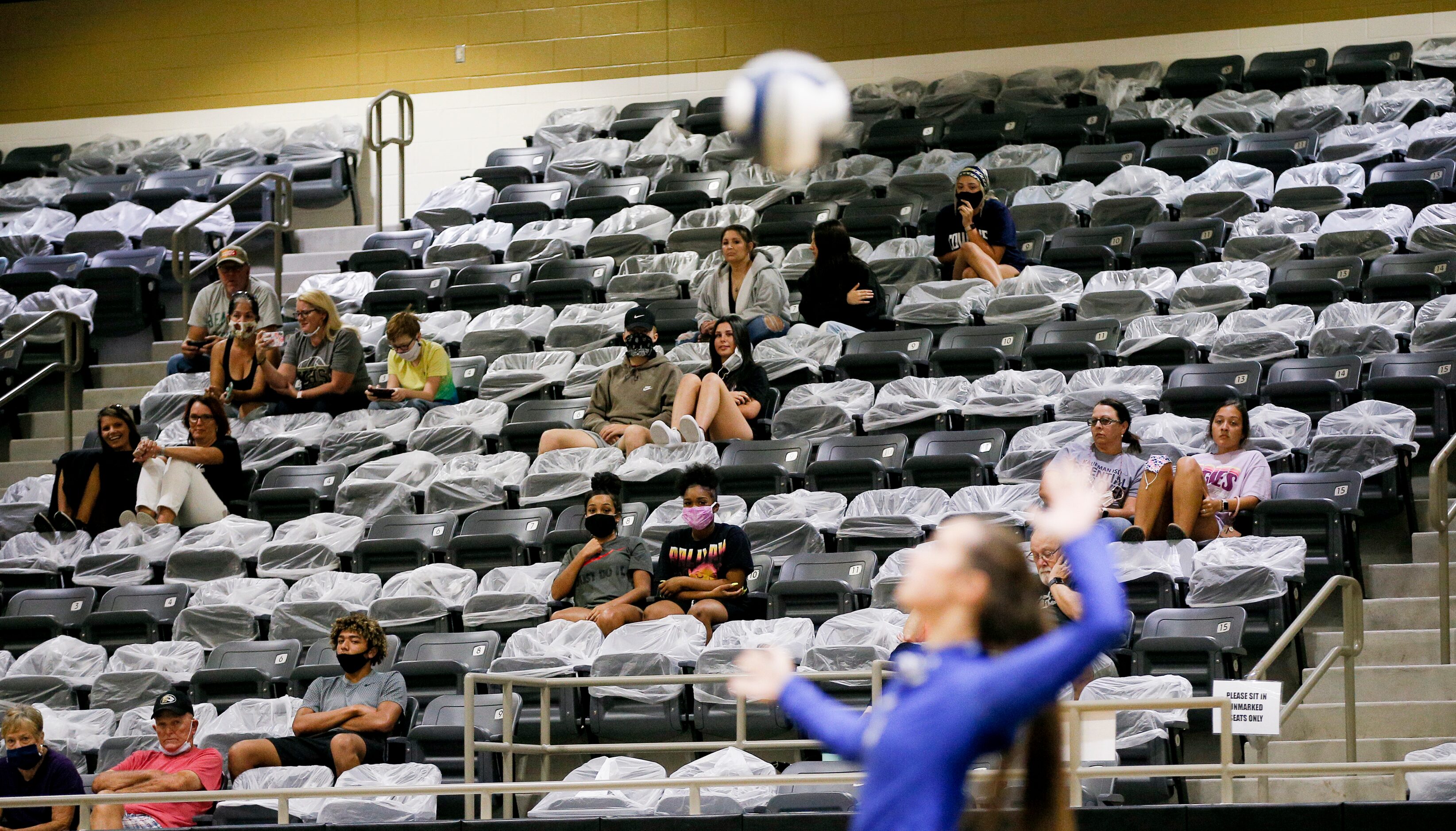 Volleyball spectators look on while social distancing with seats cordoned off with plastic...