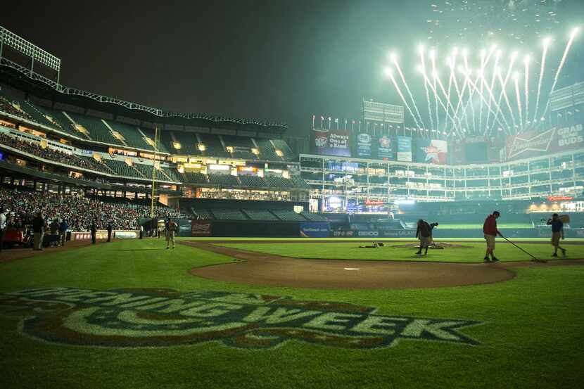 Fireworks light up the sky over Globe Life Park as groundskeepers work the field following...