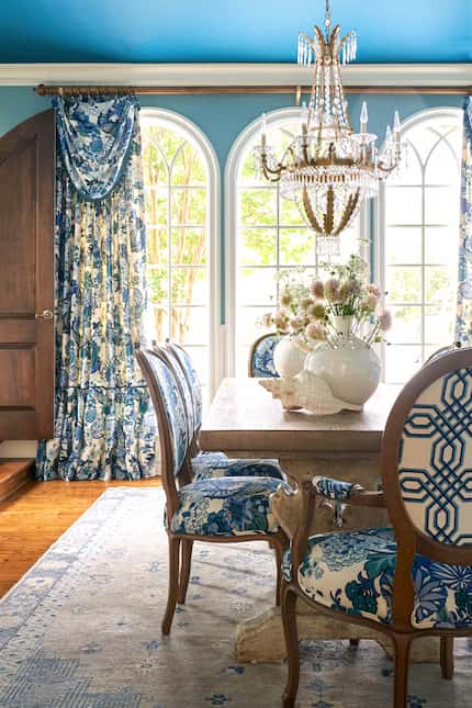 Sunny dining room with blue with blue walls and ceiling, blue and white printed curtains and...