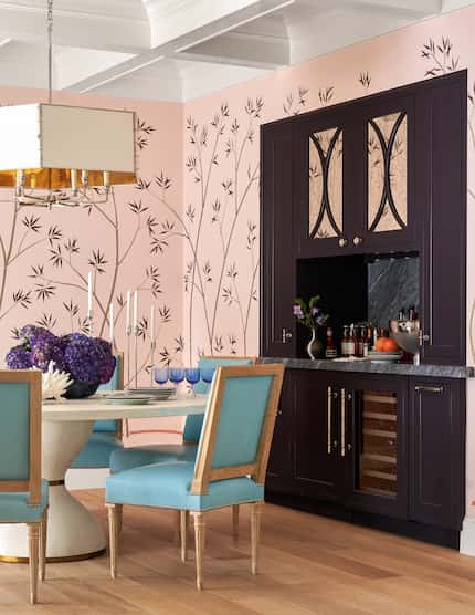 Pink dining room botanical wallpaper, dark plum cabinetry, blue chairs around round dining...