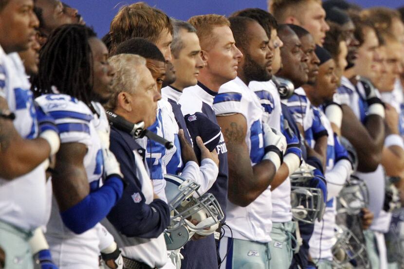 Dallas head coach Jason Garrett stands with his team during the National Anthem before the...