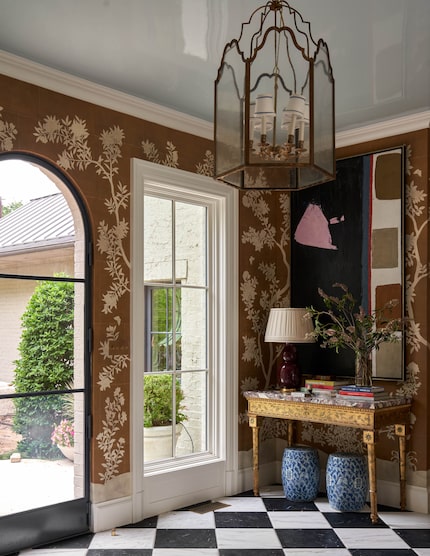 An entryway with a black-and-white tile floor, decorative wallpaper and an antique table.