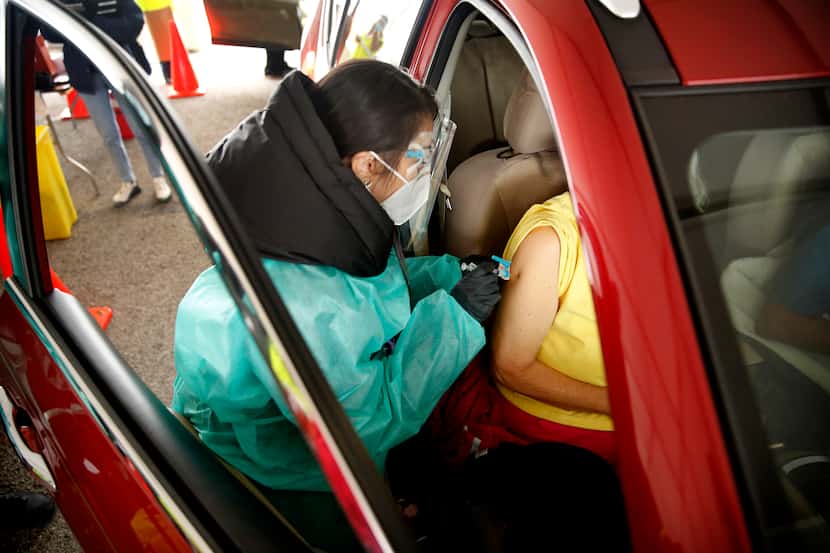 A senior receives a COVID-19 vaccination from a volunteer working the drive-thru line...