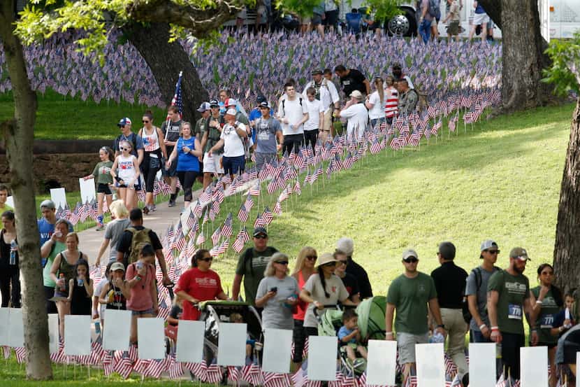 Participants walks pass flags and stories signs planted in the grass honoring police...
