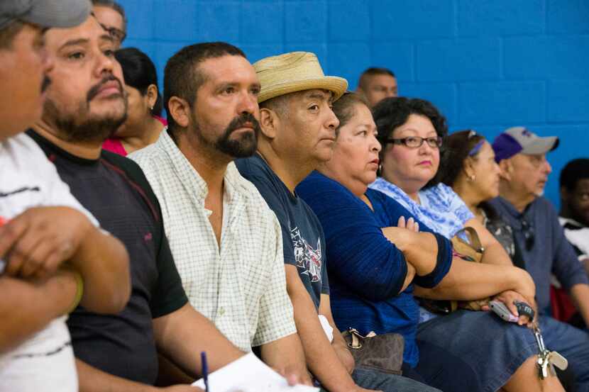 Community members listen to announcements during a community meeting regarding upcoming mass...