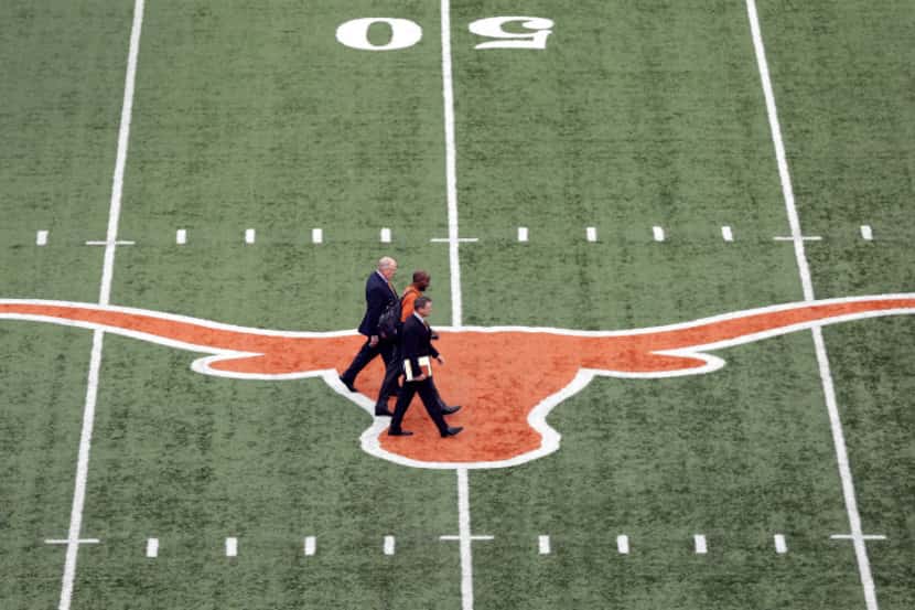 Tom Herman, center, walks across the Texas logo at Texas Memorial Stadium with associate...
