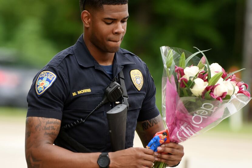 Baton Rouge police officer Markell Morris holds a bouquet of flowers and a Superman action...