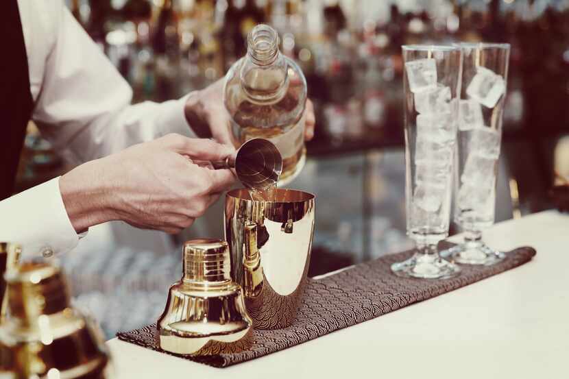 Bartender is pouring liquor in golden shaker, toned image