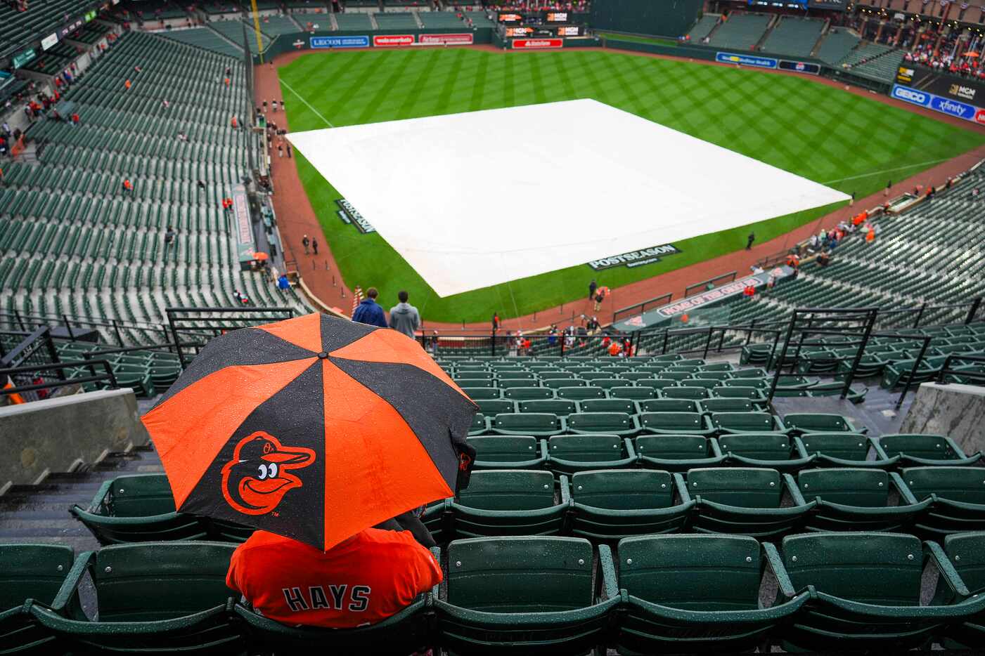 A fan takes cover from a light rain as the tarp covers the field during a rain delay prior...