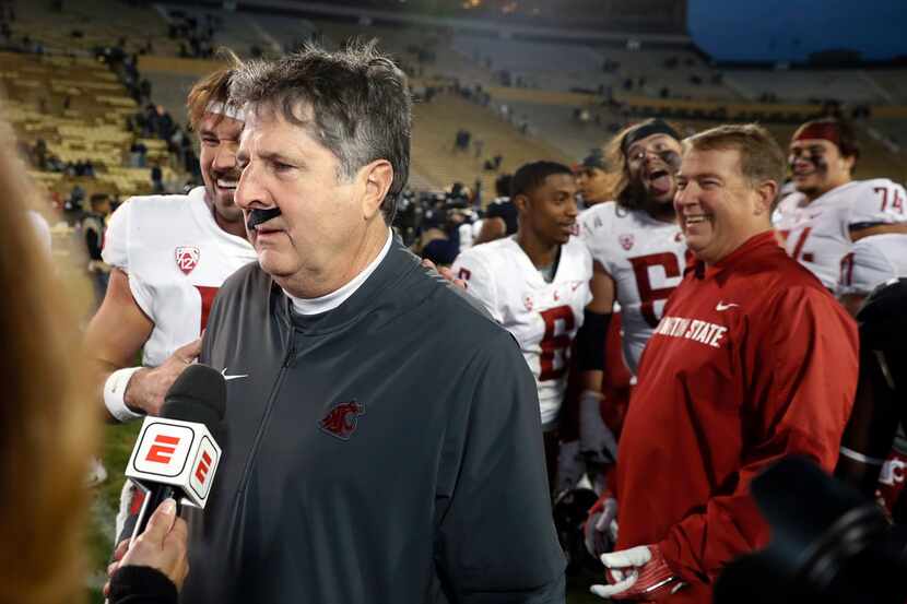 Washington State head coach Mike Leach wears a fake mustache placed on him by starting...
