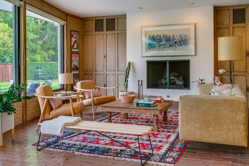 Living room with large windows, fireplace flanked by cabinetry and midcentury modern-style...