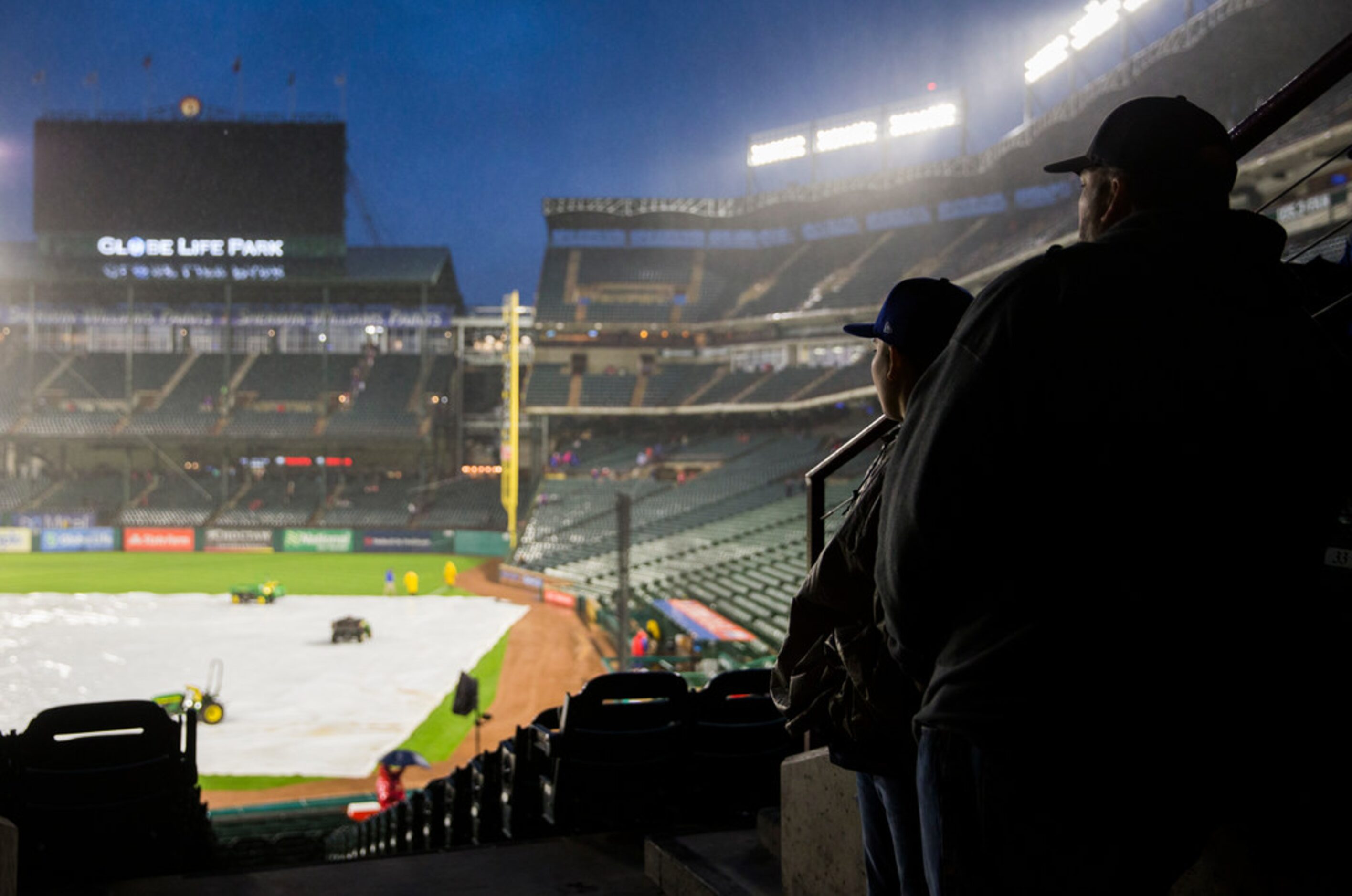 Fans watch the rain fall during a rain delay at an MLB game between the Texas Rangers and...