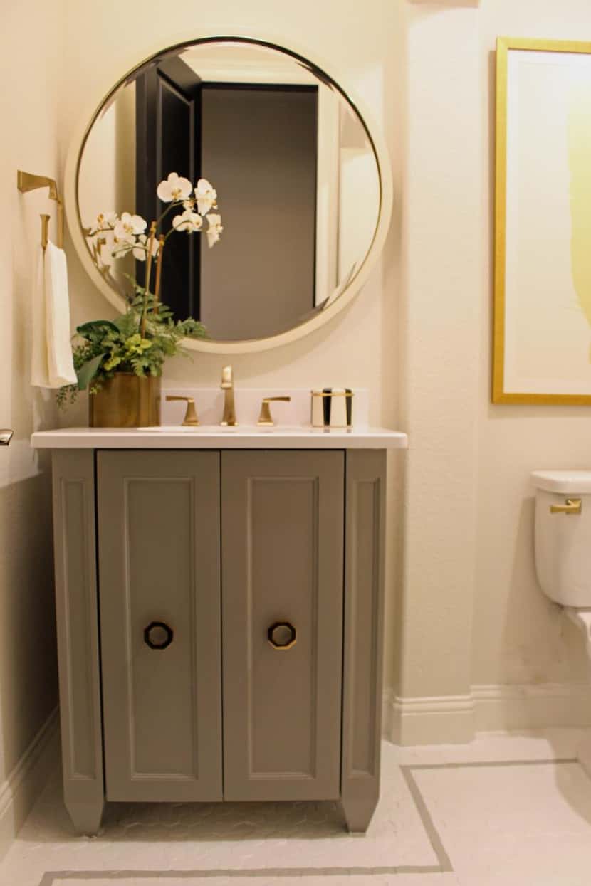 A gold-framed round mirror makes a dramatic and glamorous statement in this powder bath from...
