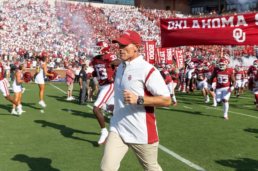 Oklahoma coach Brent Venables and players run onto the field before an NCAA college football...