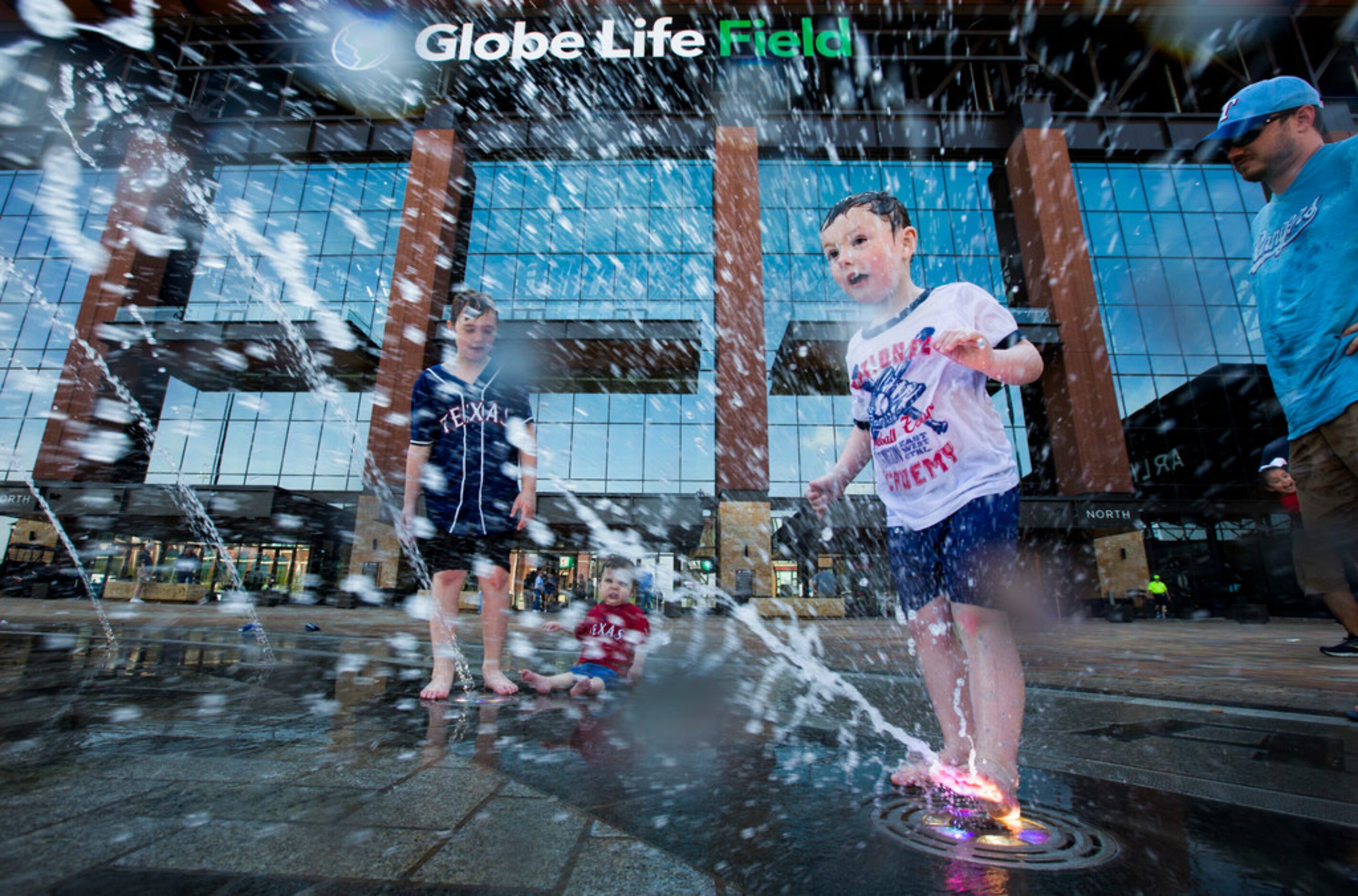 Jonah Proctor (center), 4, uses his foot to spray water from a fountain outside the Texas...