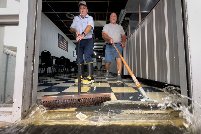 Randy Sikes, left, brooms water out of Diamond Dave's Grill as residual rain water flooding...