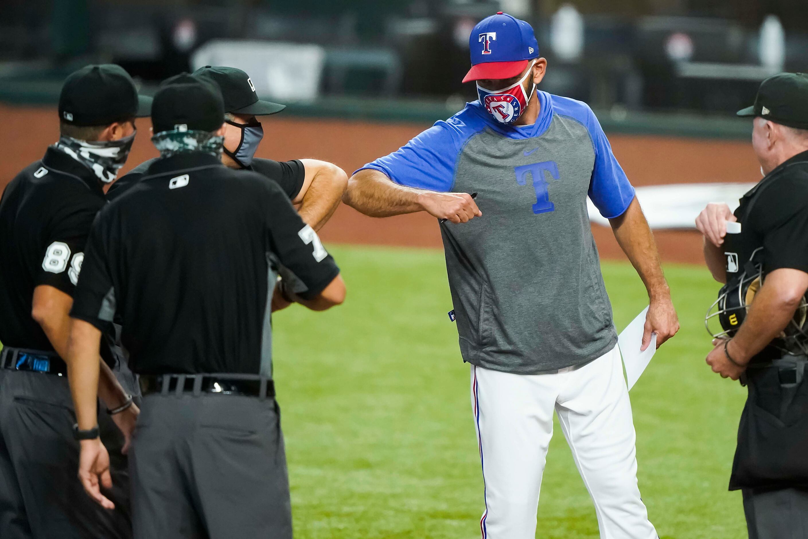 Texas Rangers manager Chris Woodward elbow bumps with umpires as he brings the lineup card...