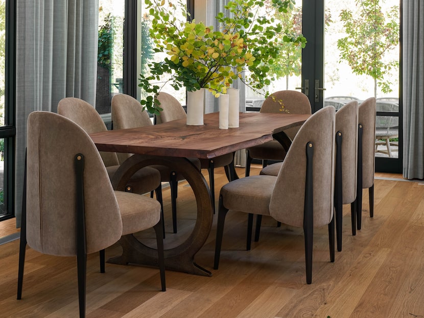 Brown dining chairs around a wooden table with a large flower arrangement.