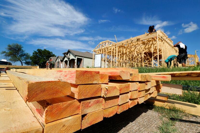 Stacked lumber sits on the sidewalk as construction workers frame out a new home along...