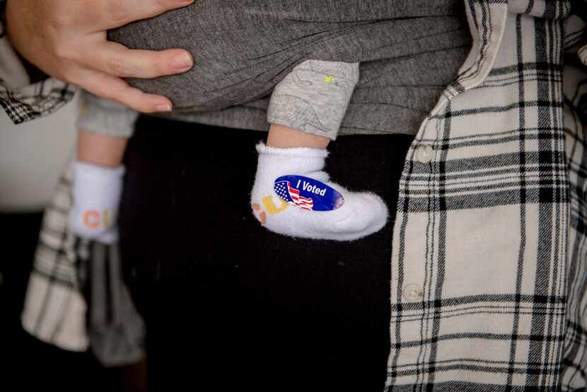 Brooke Villalpando holds her son, Maverick Aho, who has an "I voted" sticker on his sock, in...