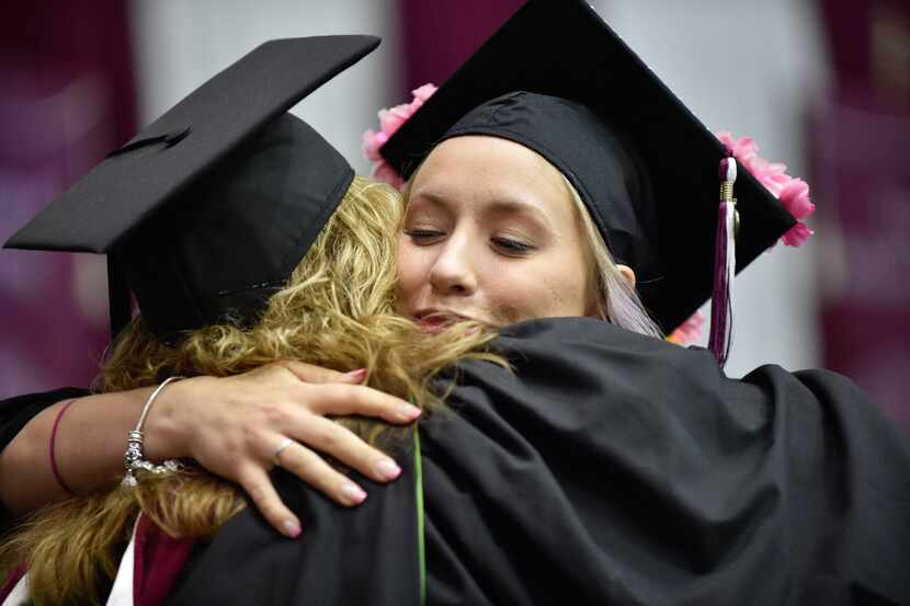 Graduating students walk the stage, receive their diplomas and embrace each other during a...
