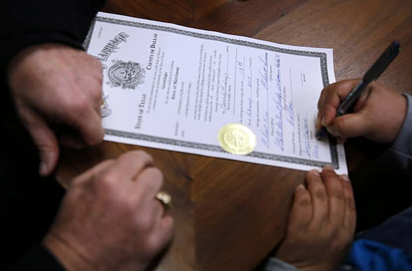 Judge Kent Sims (left) looks on as a witness signs a marriage license following a wedding in...