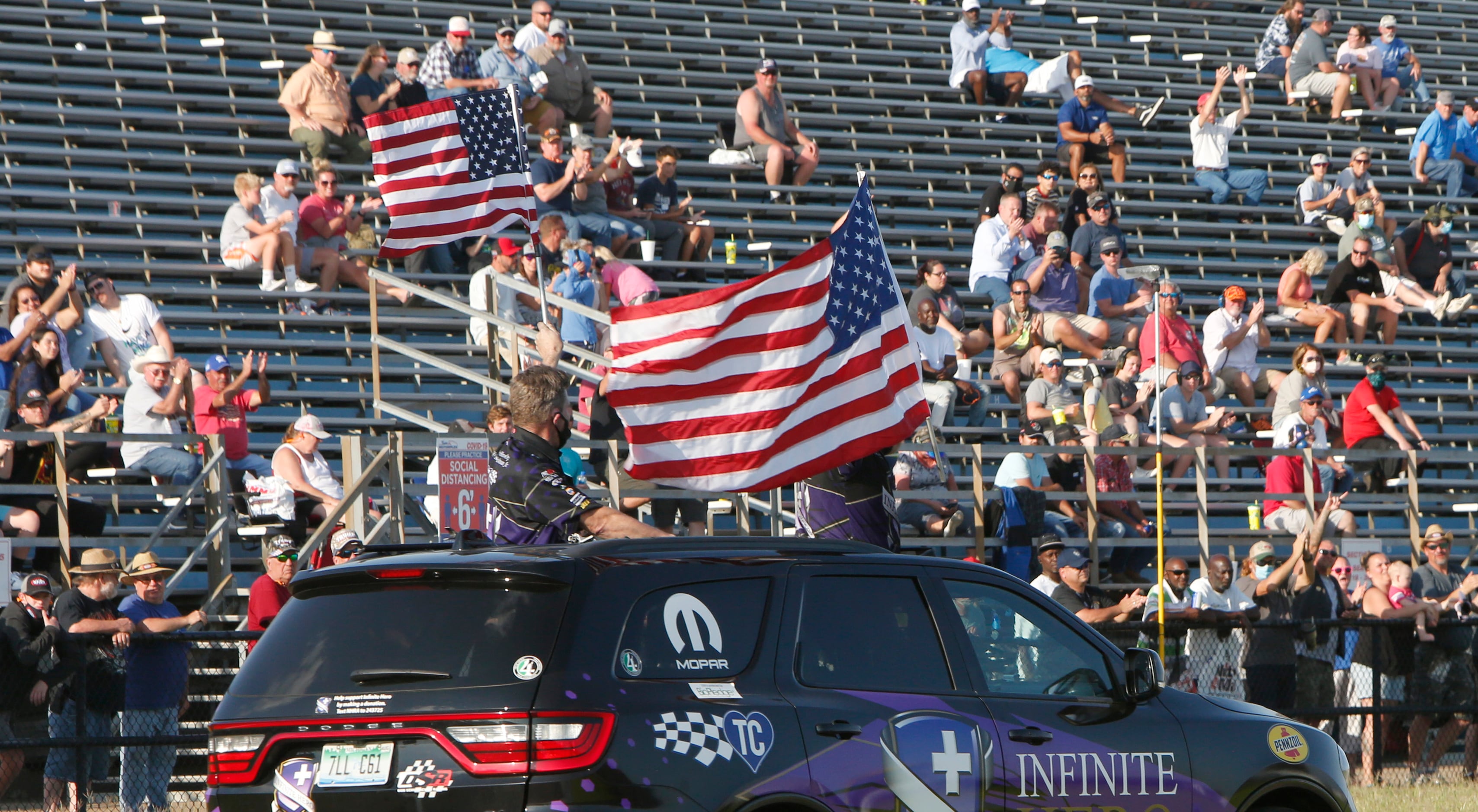 Racing fans cheer as a racing team sponsor drives around the track waving american flags....