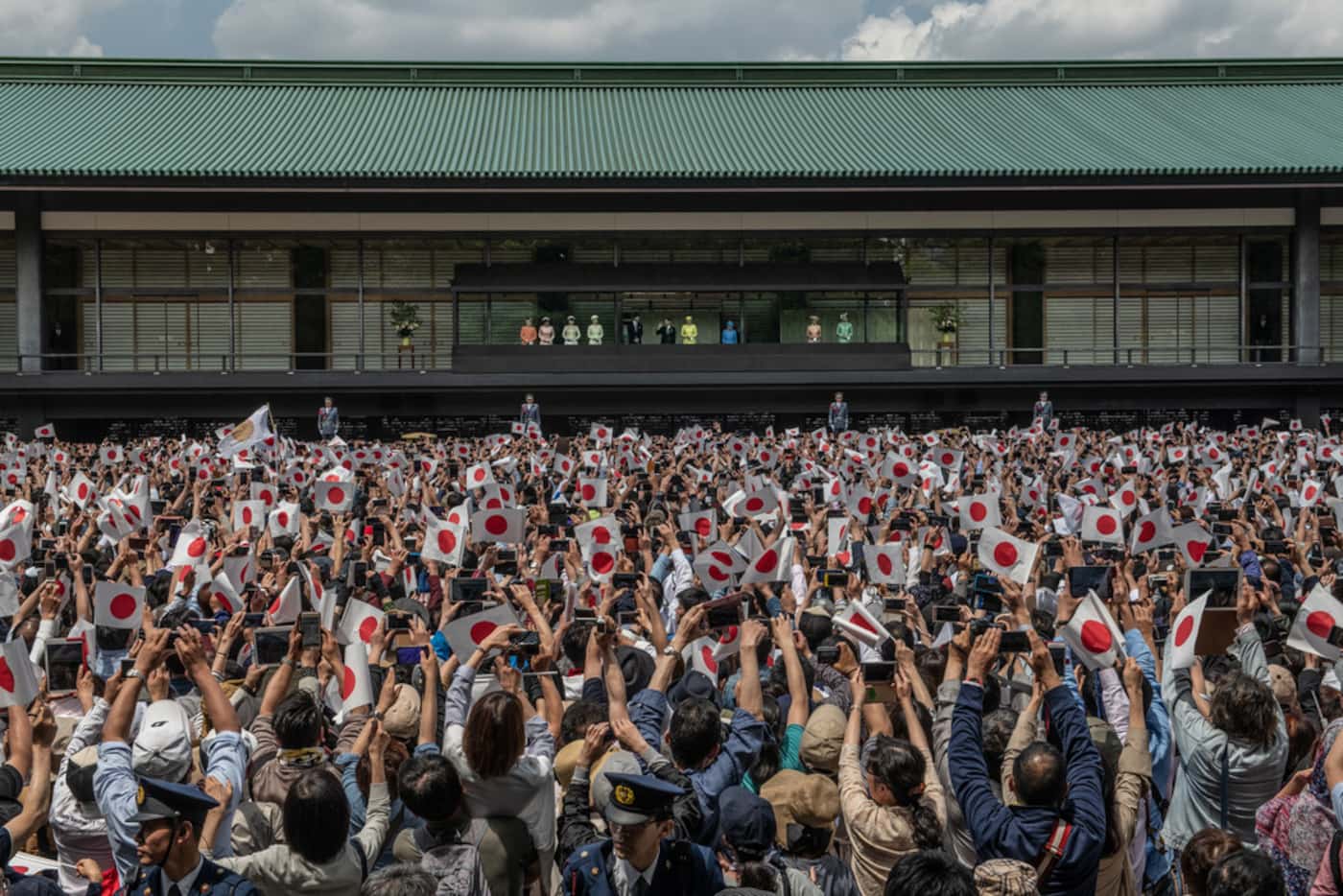 People wave Japanese flags as Emperor Naruhito of Japan waves to members of the public as...