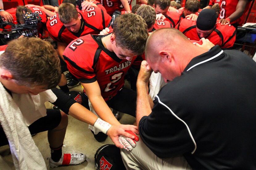 Head football coach David Woodard prayed with his varsity team in the locker room before...
