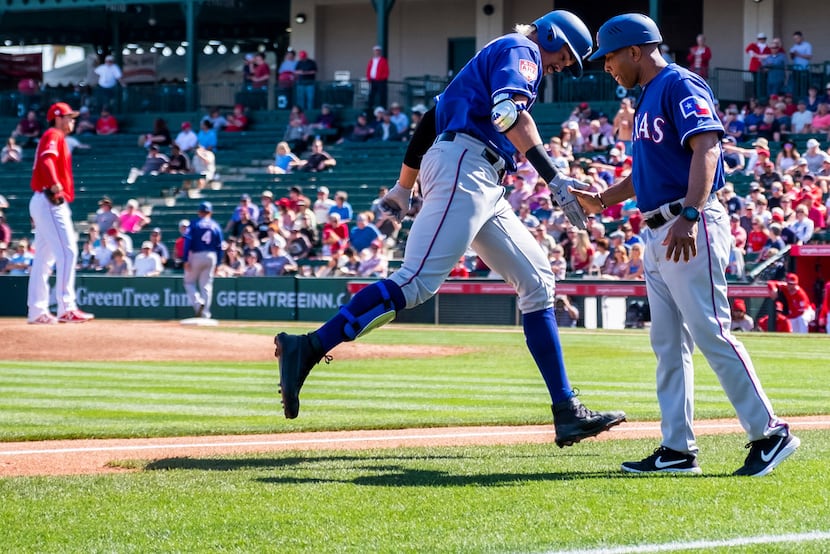 Rangers first baseman Ronald Guzman slaps hands with third base coach Tony Beasley as he...
