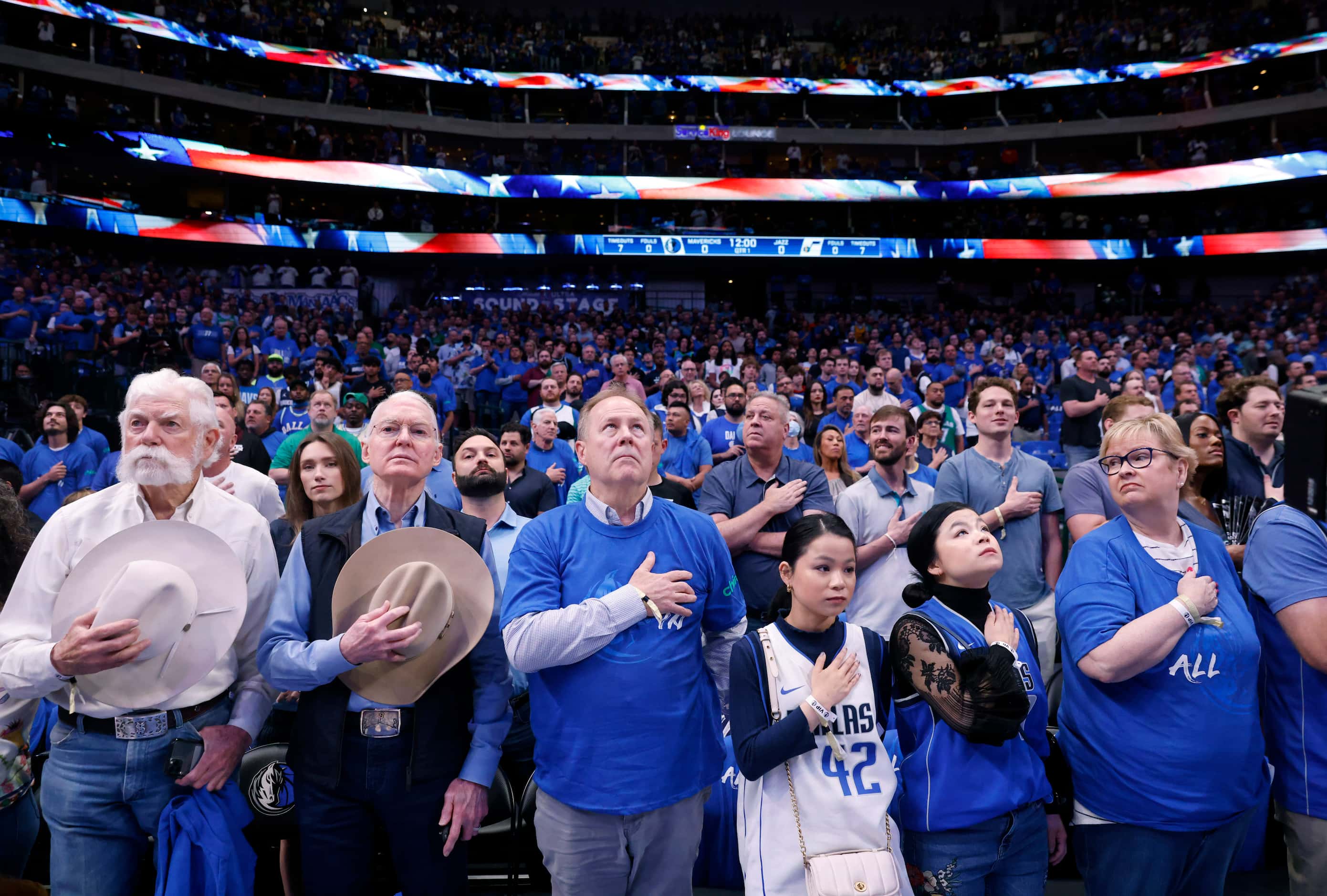 Dallas Mavericks fans, some with cowboy hats over their hearts, stand for the national...