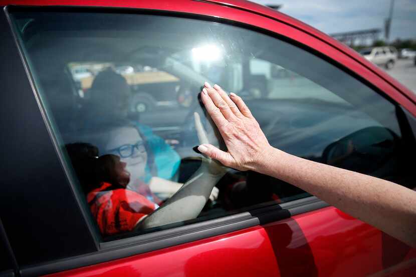 Volunteer Karen Kirk, of Houston, gives a student a high-five through the window after a...