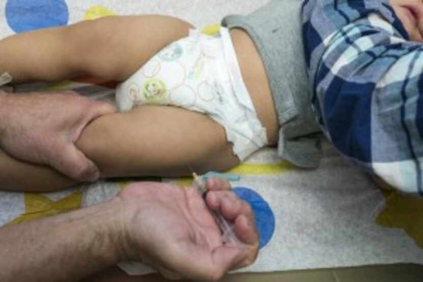  A pediatrician uses a syringe to vaccinate a 1-year-old with the measles-mumps-rubella...